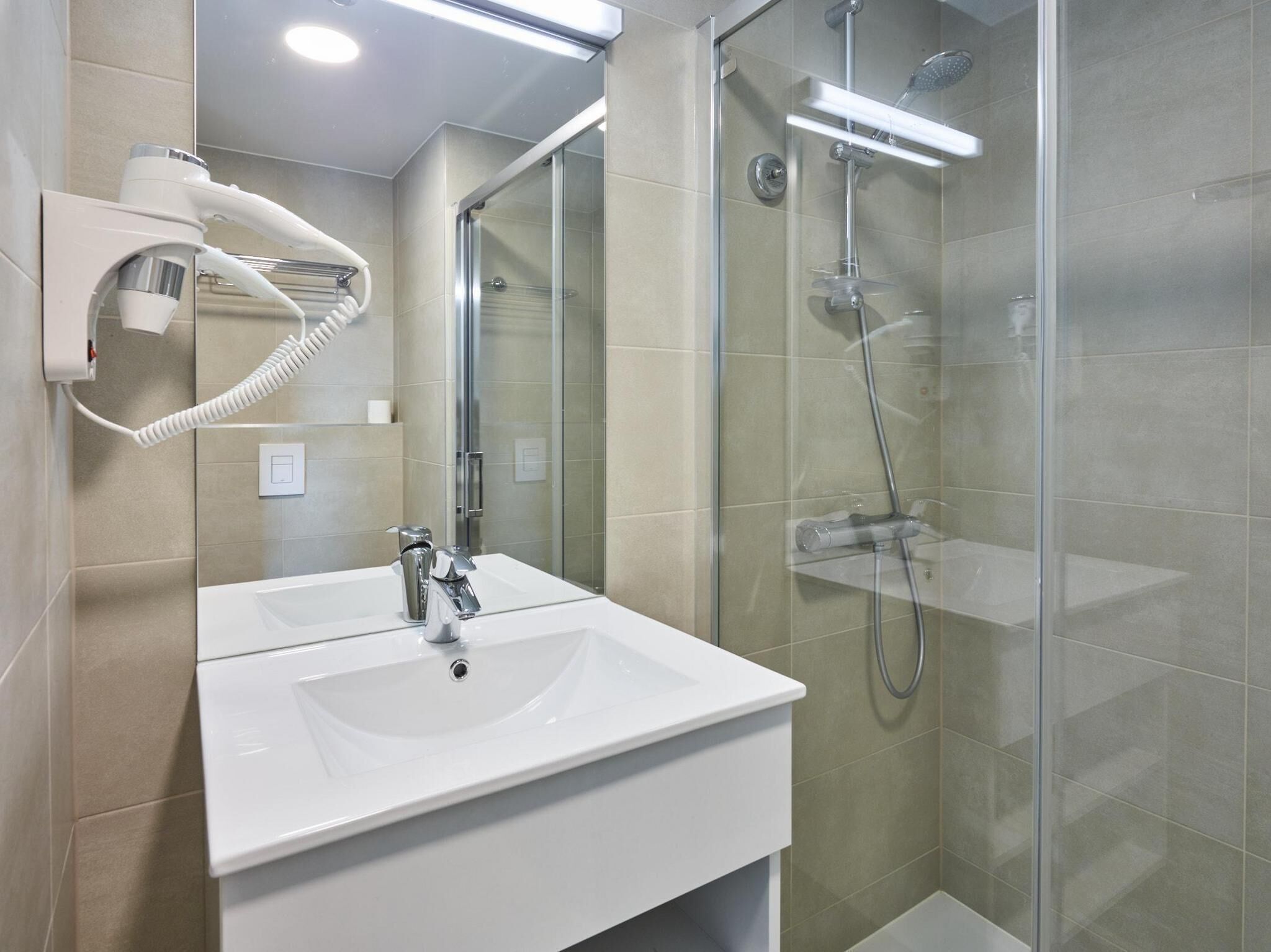 Un bagno moderno con un lavandino bianco, un asciugacapelli portatile e una cabina doccia in vetro.