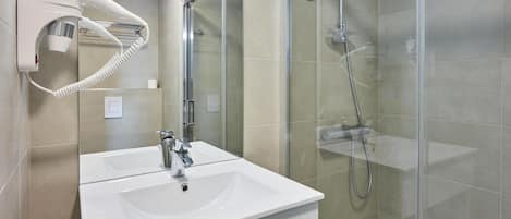 Un bagno moderno con un lavandino bianco, un asciugacapelli portatile e una cabina doccia in vetro.