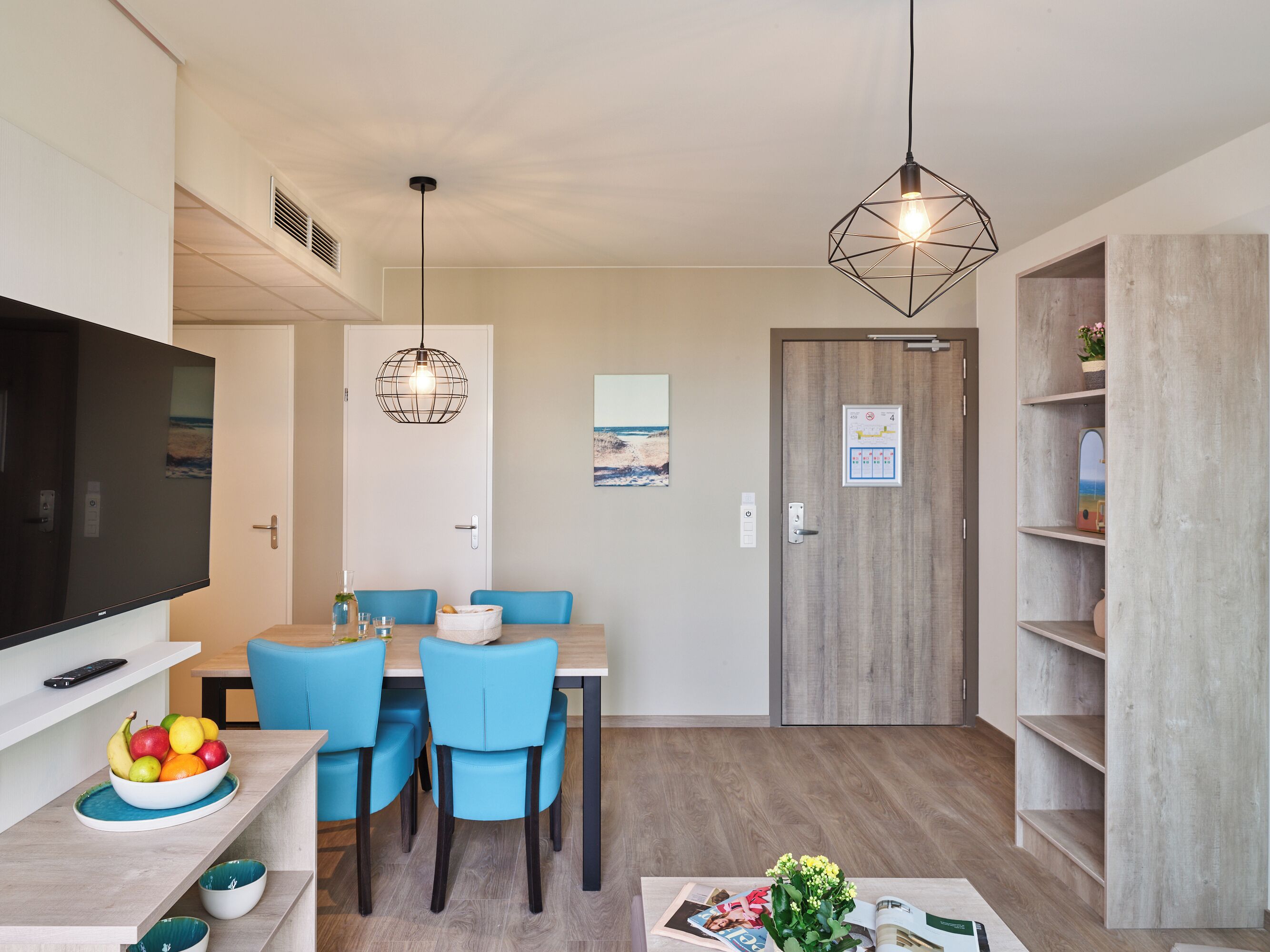 A modern living room with a dining area, a television, and a wooden bookshelf.