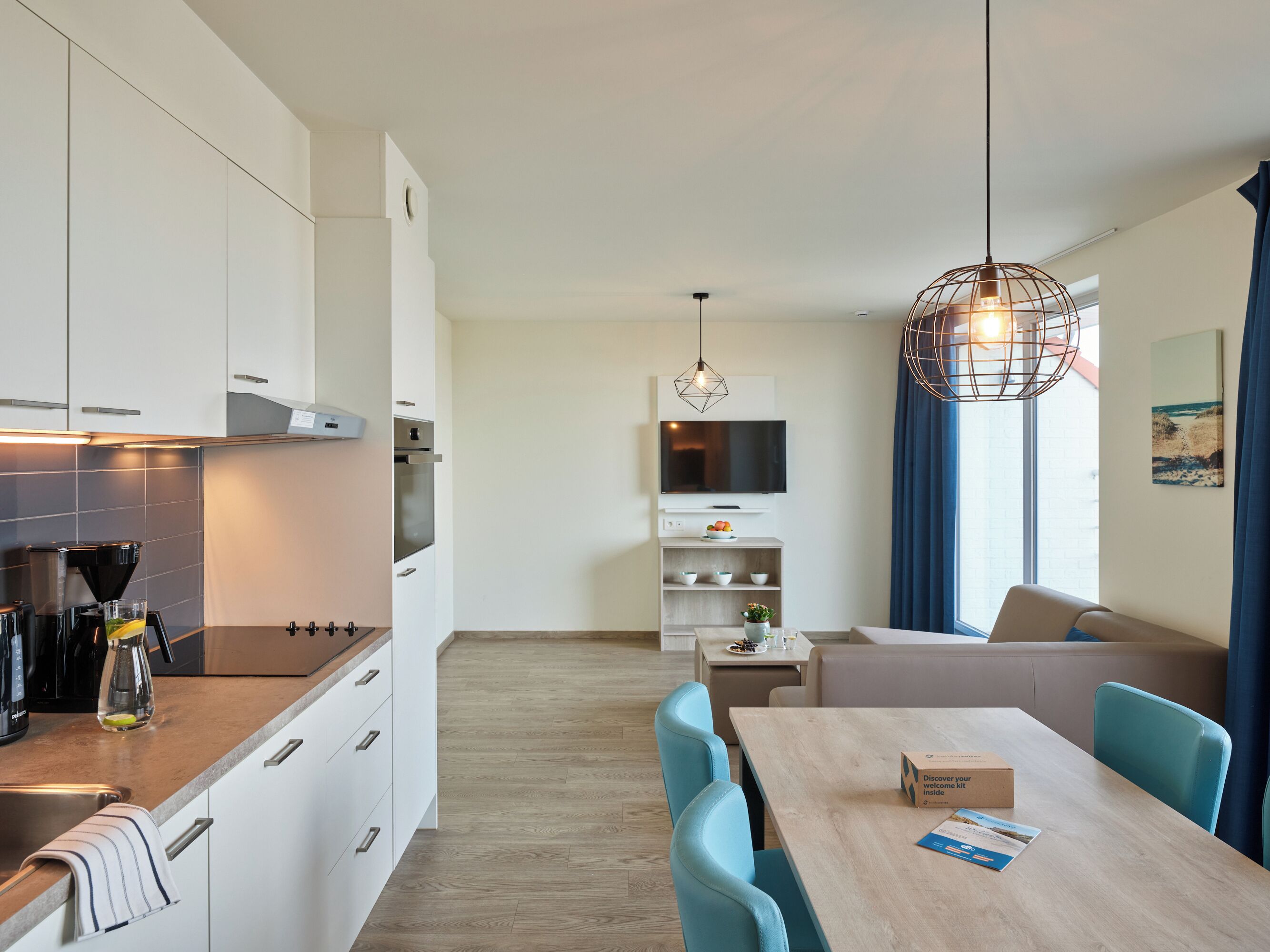 A modern kitchen with white cabinets, a coffee machine, and a dining area with a table and chairs.