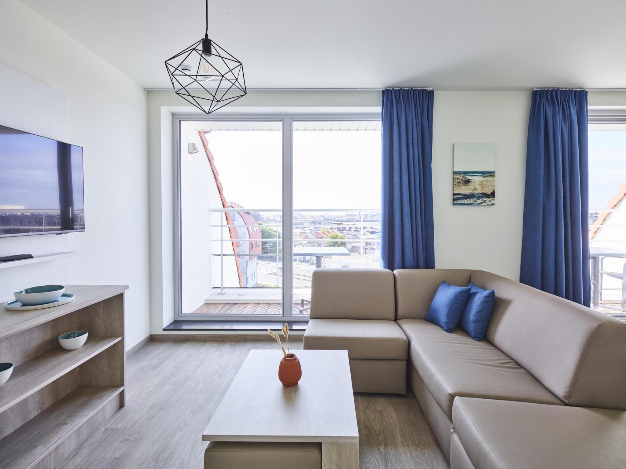 Un salon moderne avec un canapé, une table basse, un téléviseur et un balcon offrant une vue sur la ville.