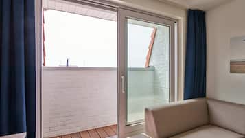 Una habitación con una puerta corrediza de vidrio que da a un balcón con pared de ladrillo blanco y suelo de madera.