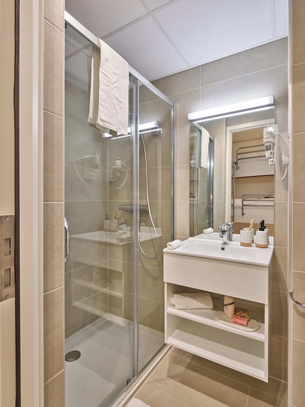 A modern bathroom with a glass-enclosed shower, a white sink with a mirror above, and a towel rack. - Holiday Suites Zeebrugge (Bruges)