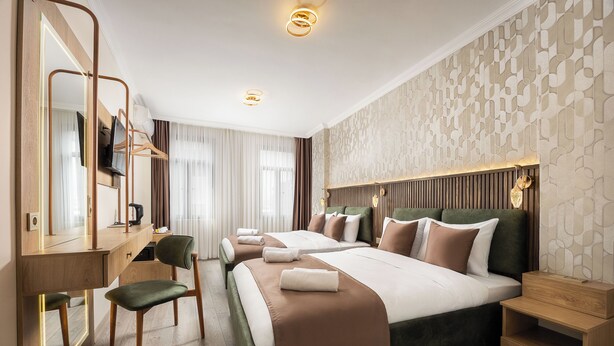 Habitación de hotel con dos camas, un escritorio con espejo, una silla, una mesita de noche y una pared con diseño geométrico.