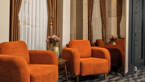 Un vestíbulo de hotel con piso a cuadros, un área de descanso con sillones tapizados en naranja, un florero con flores y un espejo grande que refleja la habitación.