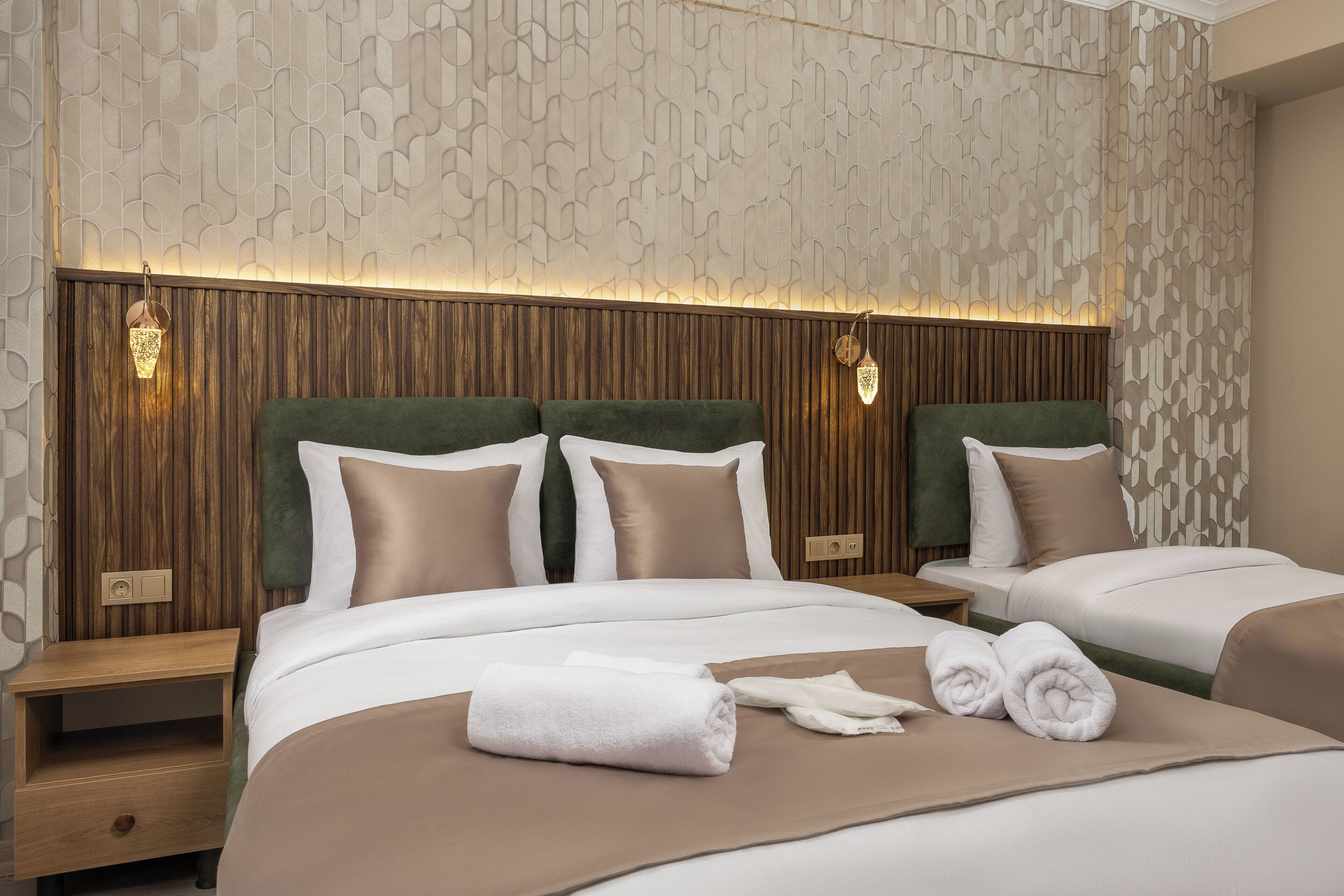 Quarto de hotel com duas camas, cabeceiras de madeira, papel de parede estampado e abajures.