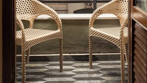 Un balcón con dos sillas de mimbre, un toldo rojo y un edificio con detalles ornamentales y una ventana.