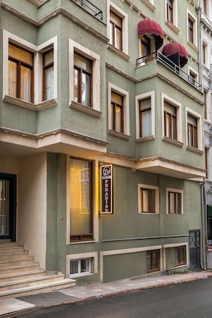 Un edificio de varios pisos con fachada verde, múltiples ventanas y una entrada visible con escalones.