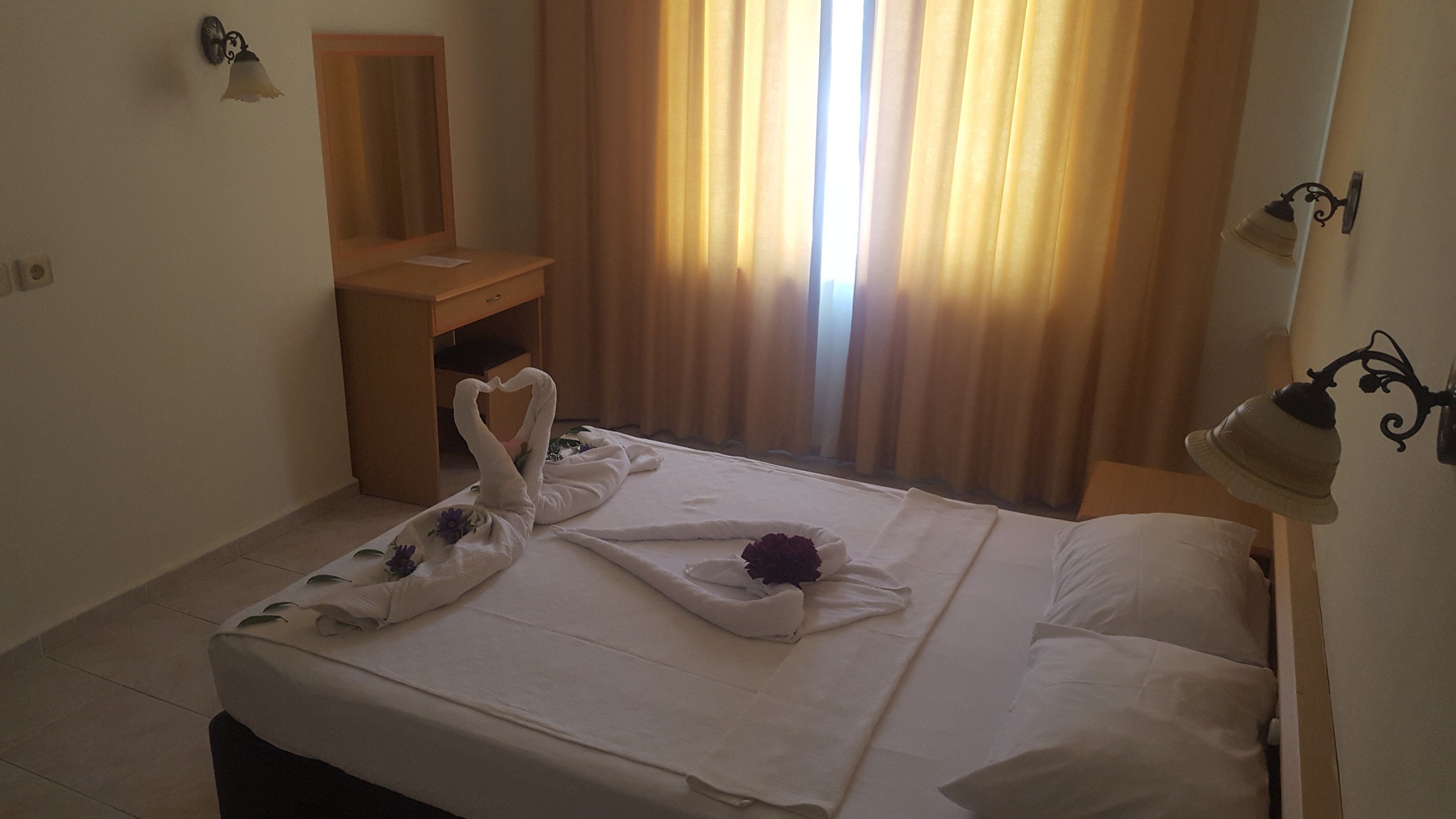 Una habitación de hotel con cama, escritorio, espejo y cortinas.