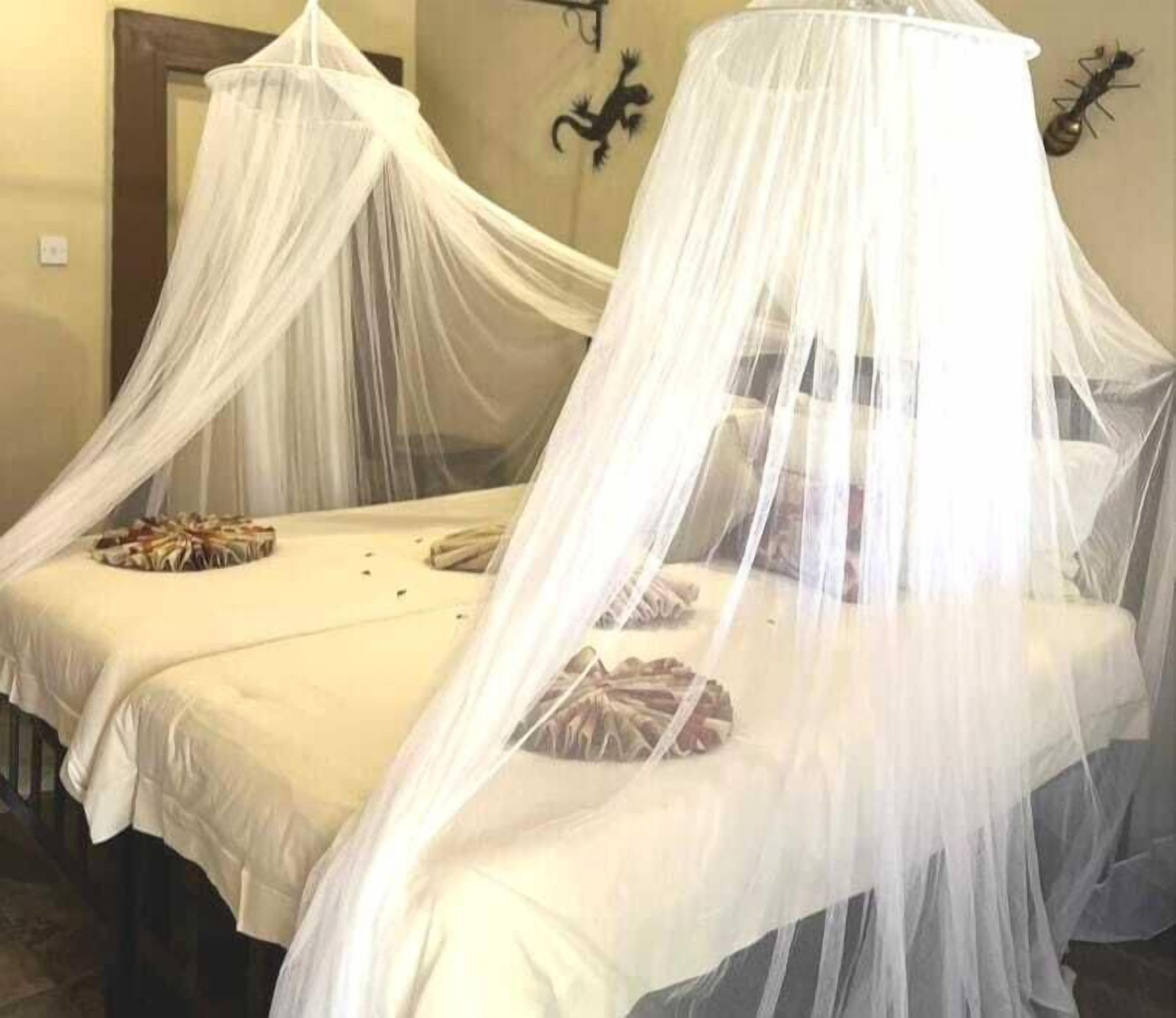 Habitación con dos camas cubiertas por dos doseles blancos, una mesa redonda con un adorno y una escultura en la pared.