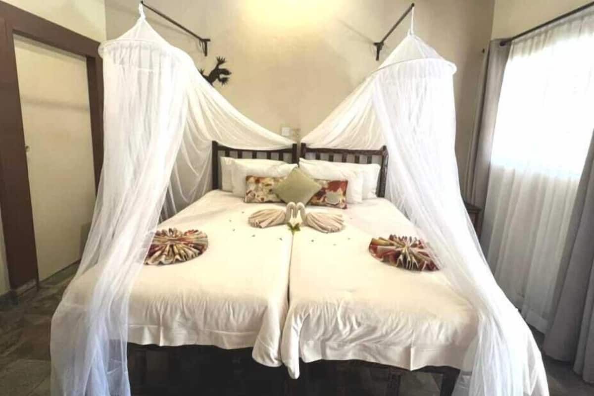 A double bed with a canopy, two pillows, and a decorative pillow on the headboard.