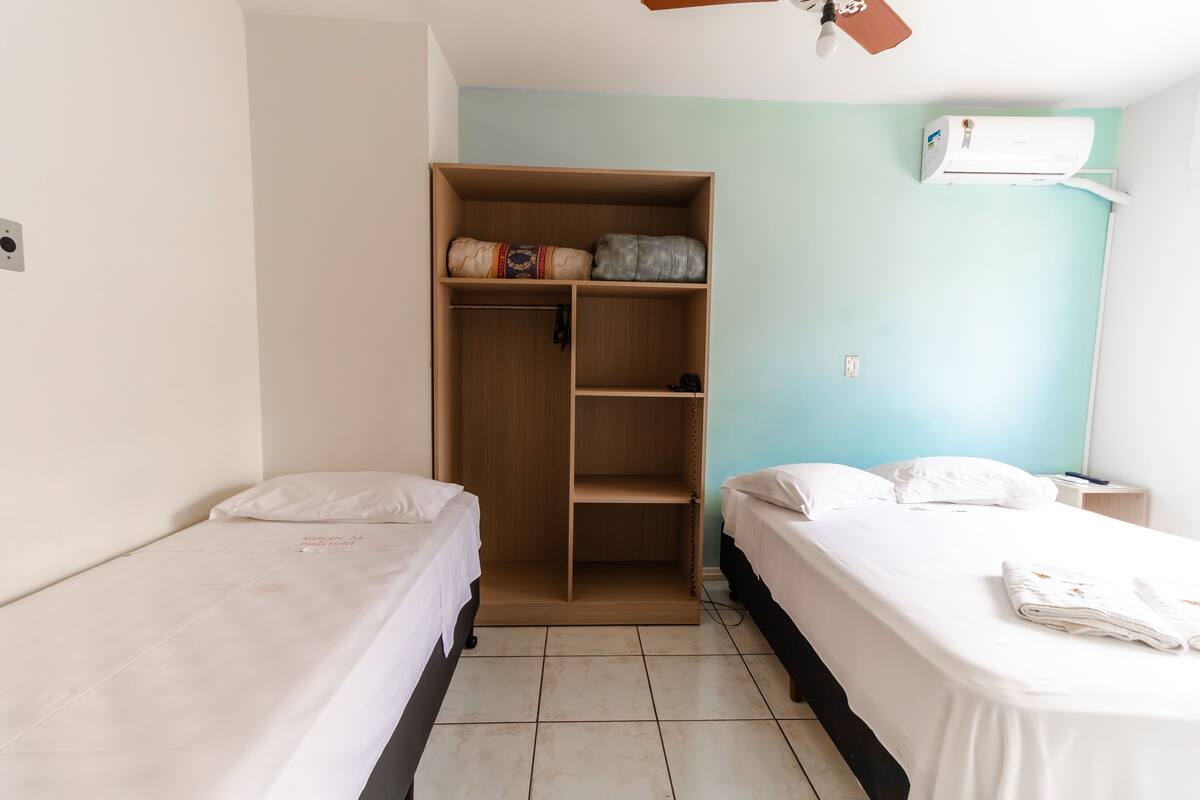 Une chambre avec deux lits, une armoire en bois et un appareil de climatisation.
