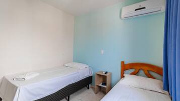 Quarto com duas camas, uma pequena mesa de cabeceira de madeira e um ar condicionado na parede.
