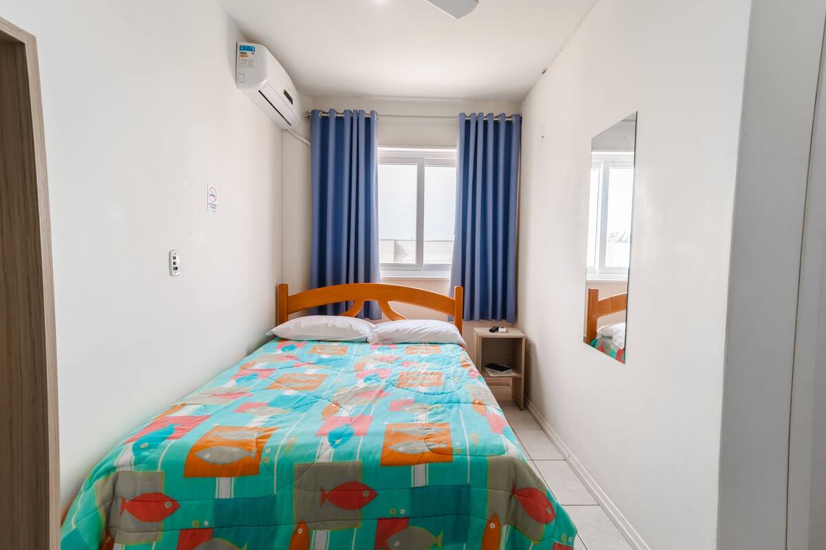 Une chambre à coucher avec un lit, une table de chevet, un miroir et une fenêtre avec des rideaux.