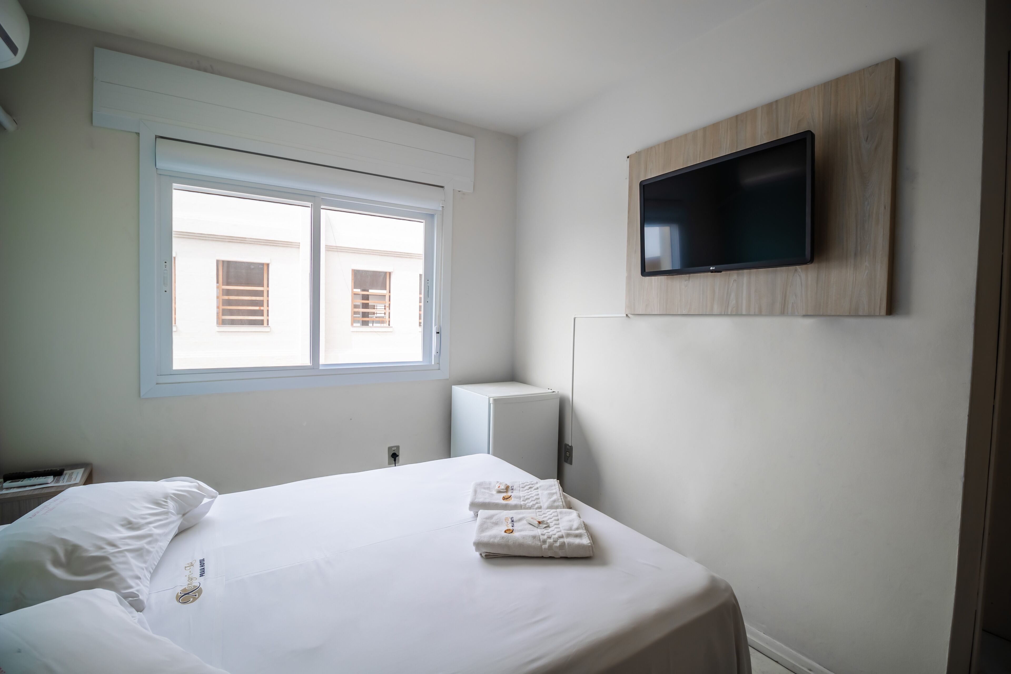 A hotel room with a bed, a TV mounted on the wall, a window, and a radiator.