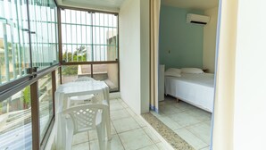Un balcon avec une table et des chaises, un lit avec un matelas et des oreillers blancs, et une fenêtre avec des barreaux en métal.