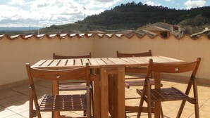 Ein Holztisch und Stühle auf einer gefliesten Terrasse mit Blick auf eine hügelige Landschaft.