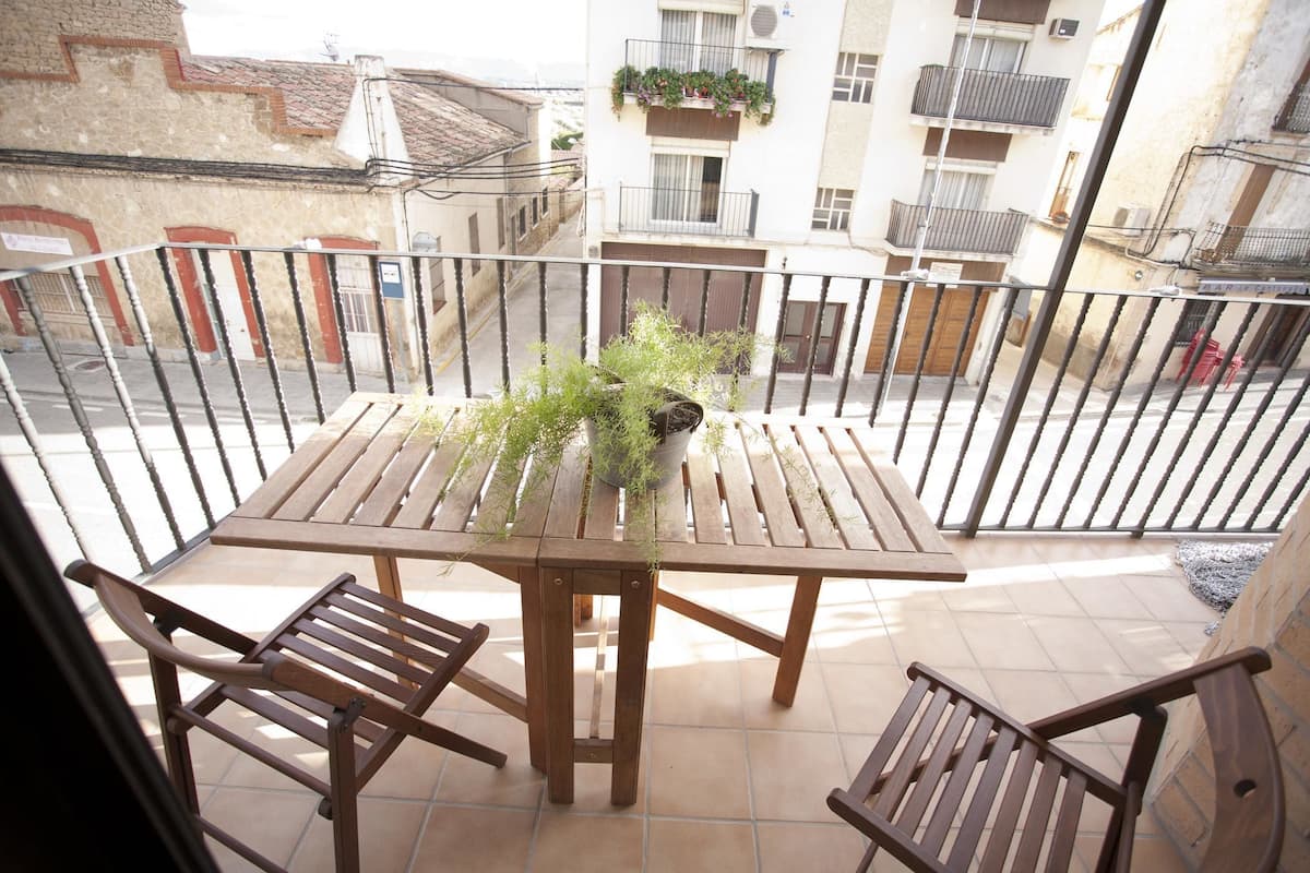 A wooden table with two chairs on a balcony with a metal railing.