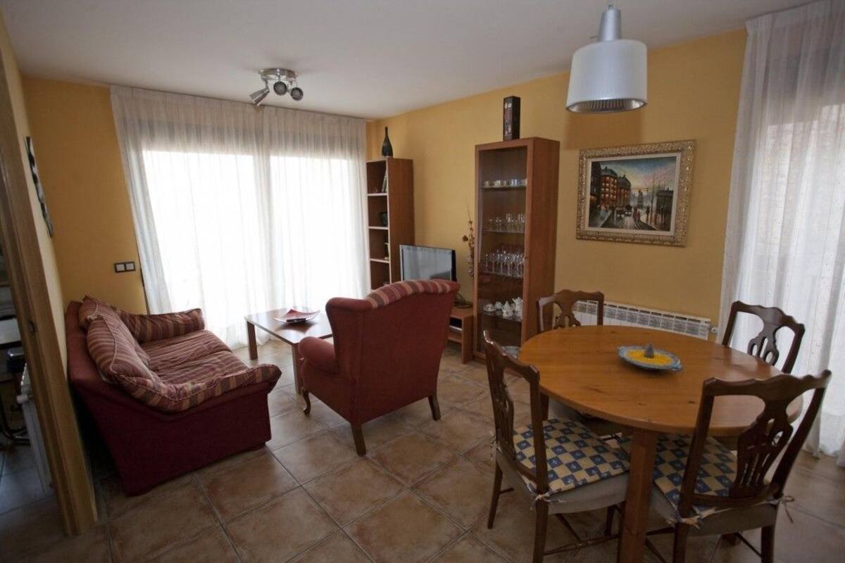 A living room with a sofa, armchair, wooden dining table, chairs, a bookshelf, and a painting on the wall.