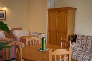 A hotel room with a wooden dining table, two single beds, a sofa, and a large wooden wardrobe.