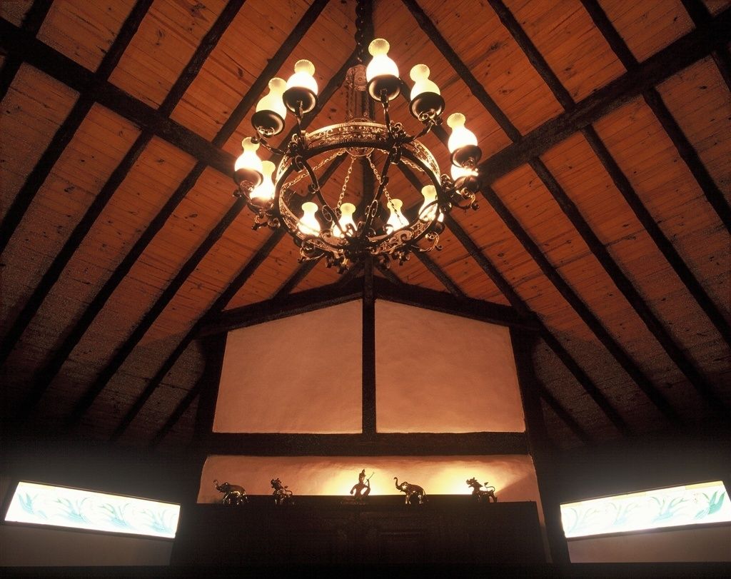 A chandelier with multiple lights, wooden beams on the ceiling, and a display case with animal figurines.