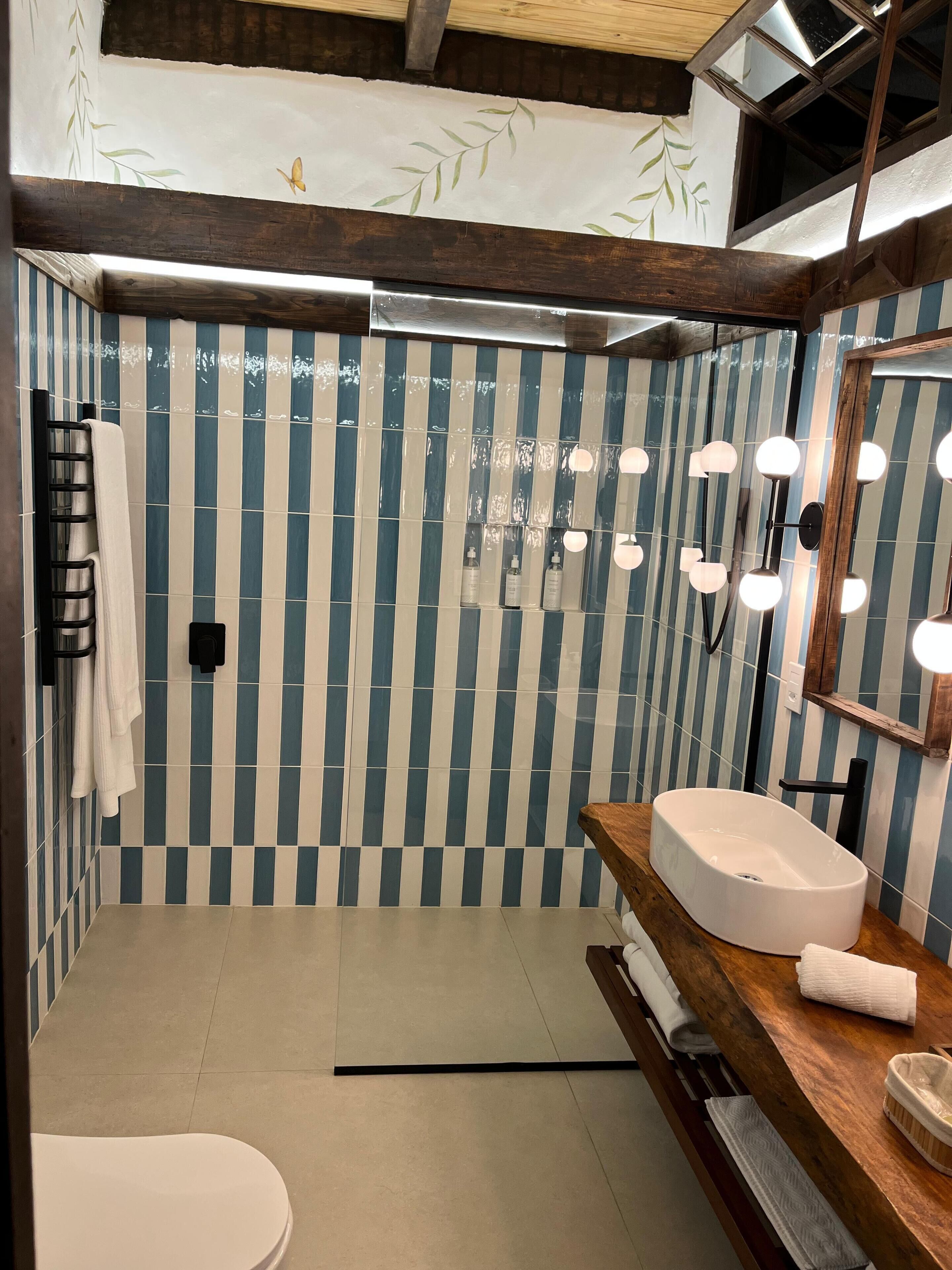 Een moderne badkamer met gestreepte wandtegels, een houten wastafelmeubel, een witte wasbak en een grote spiegel.