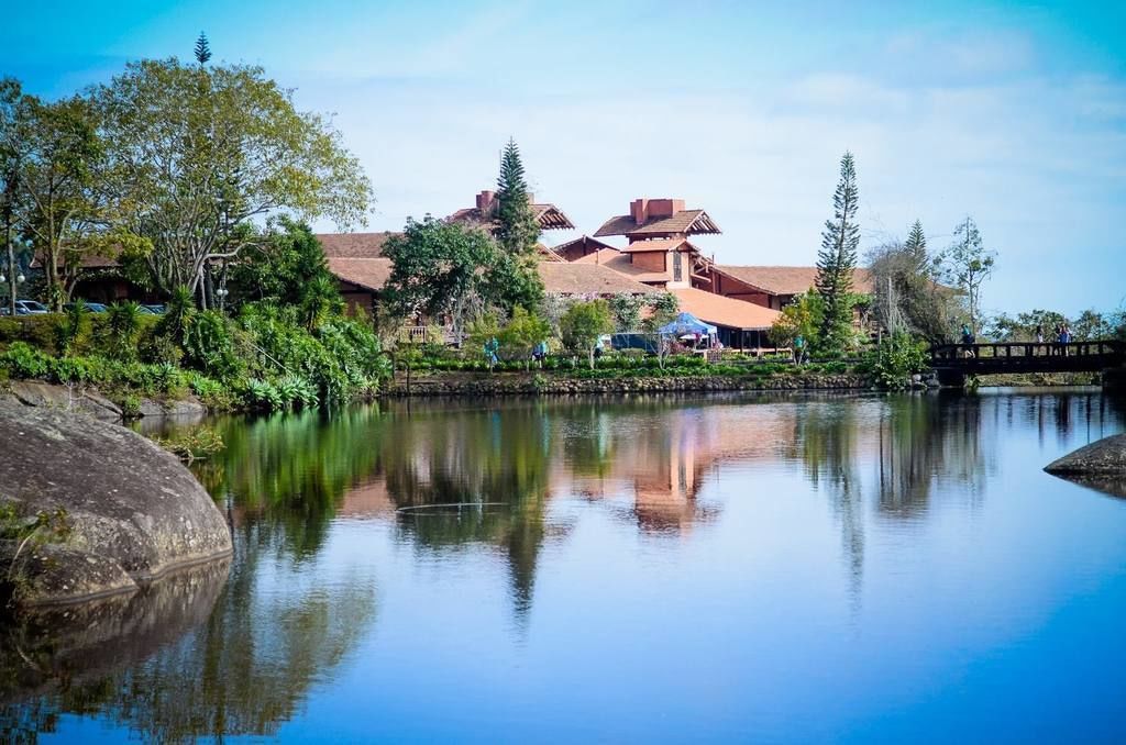 Vista serena de un lago con arquitectura tradicional, un puente y abundante vegetación.
