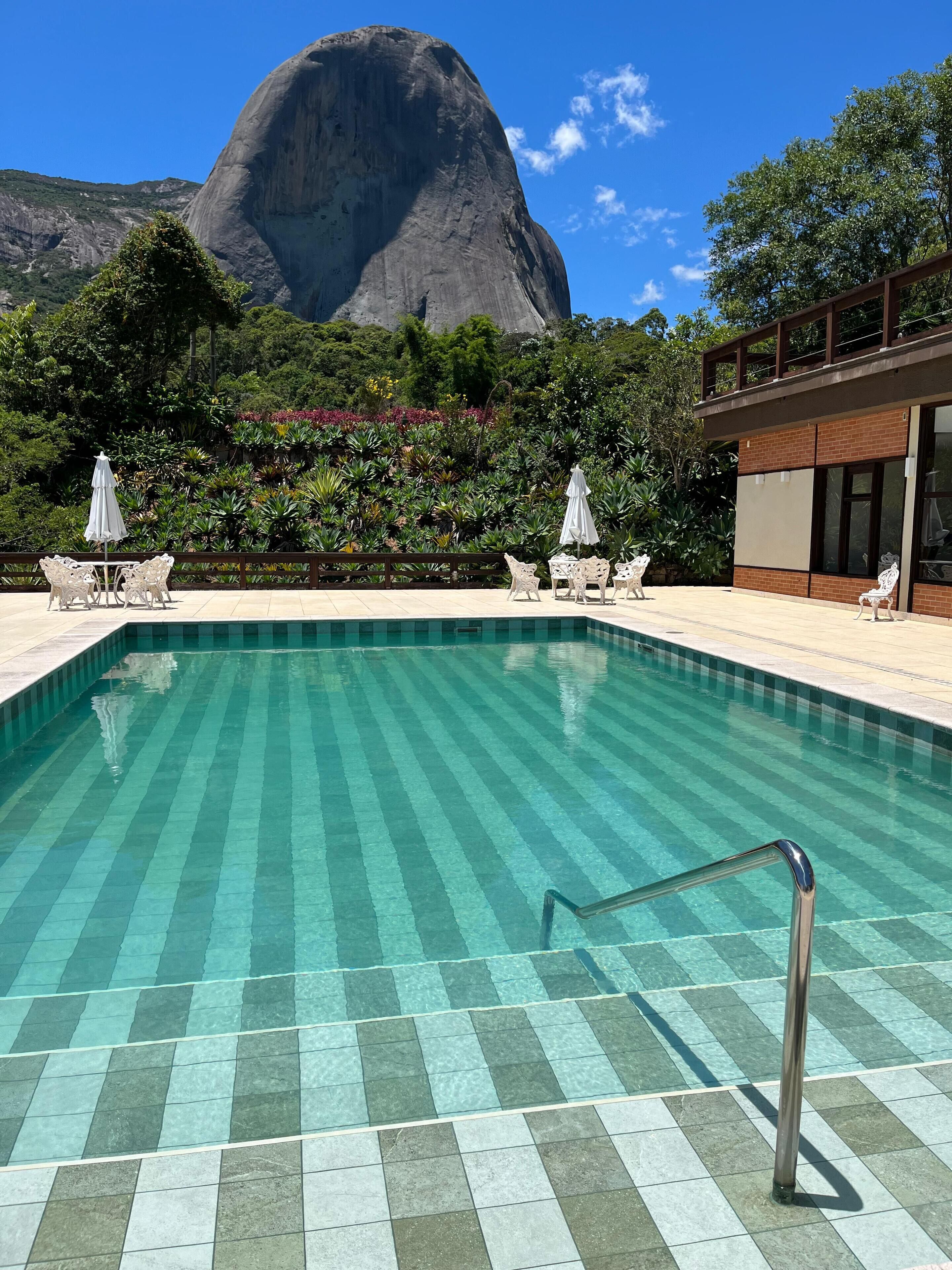A swimming pool with a view of a large mountain, surrounded by lush greenery and outdoor seating.