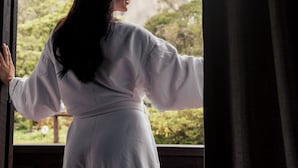 A person in a white robe standing by a window with a view of a large rock formation. - Pousada Pedra Azul (Domingos Martins)