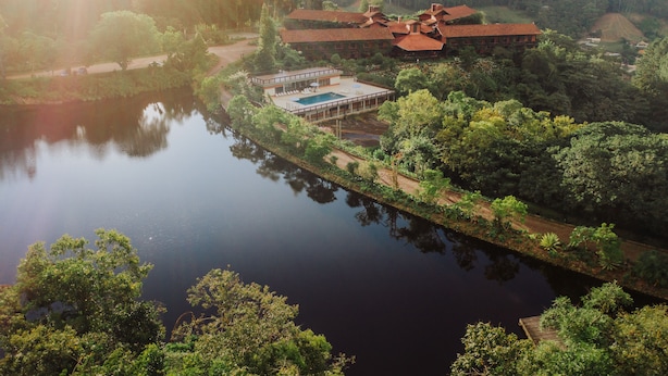 A lakeside property with a swimming pool, a covered patio, and a large house with a red roof. - Pousada Pedra Azul (Domingos Martins)