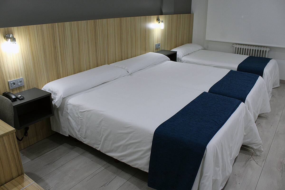 A hotel room with two beds, wooden headboard, bedside tables, and a wall-mounted light.