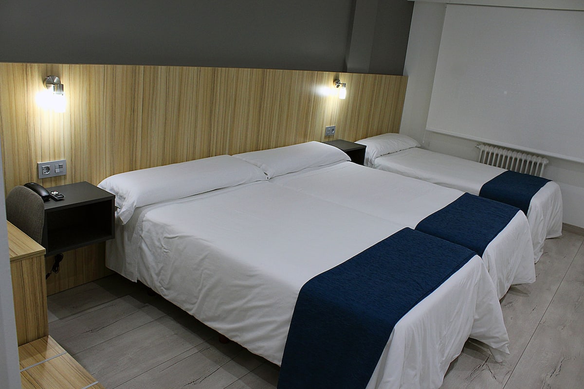 A hotel room with a large bed, bedside tables, and a wall-mounted light fixture.