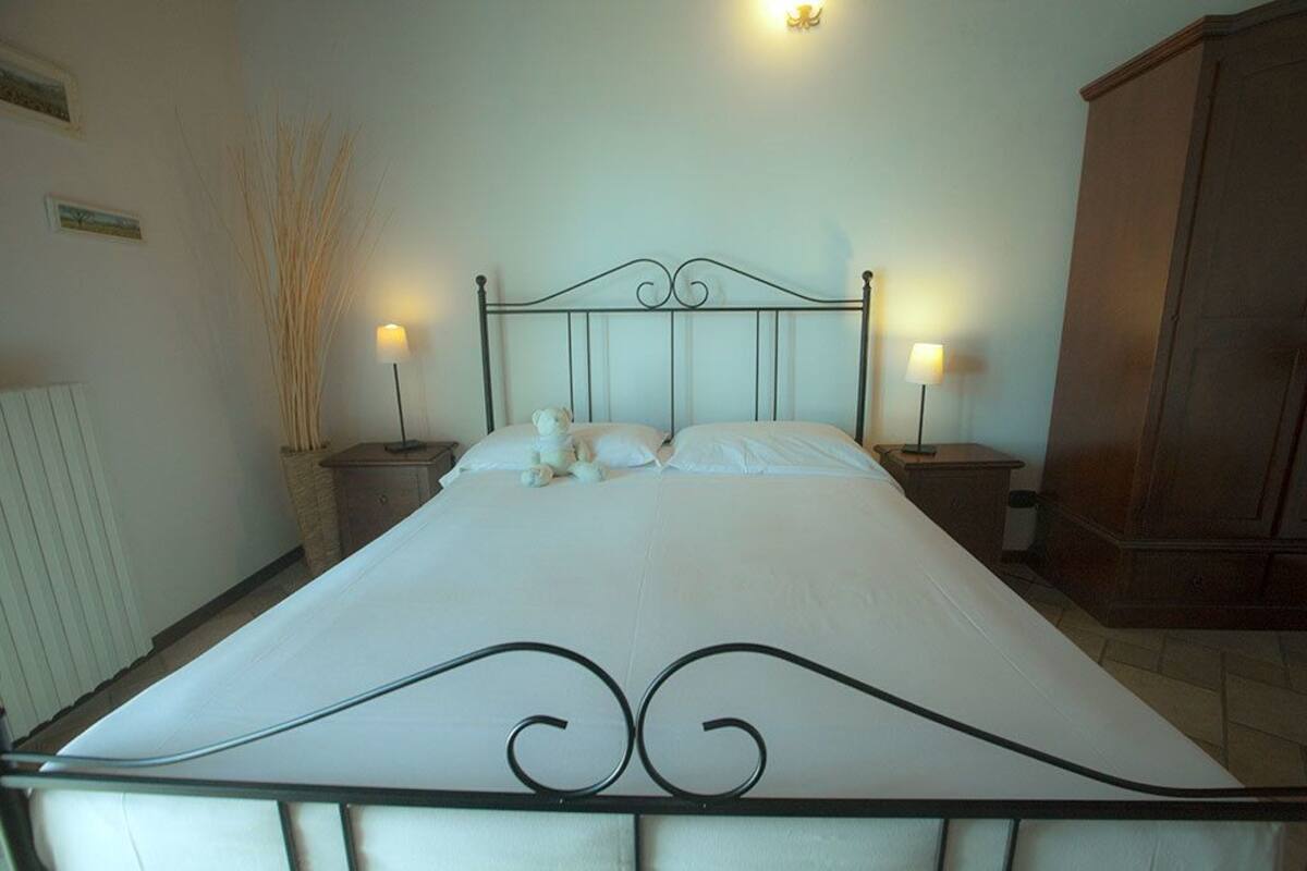 A neatly made bed with a metal headboard, two bedside tables with lamps, and a wooden wardrobe.