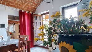 A dining area with a table set for two, a red curtain, and a large potted plant with yellow flowers. - Cà Borgo Vecchio (Brusasco)