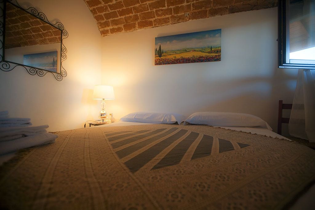 A cozy bedroom with a bed, a lamp, a painting, and a window.
