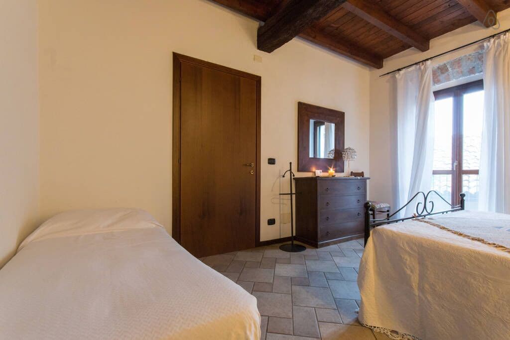 A bedroom with two beds, a wooden door, a dresser, a mirror, and a window with curtains.