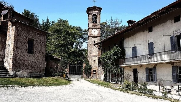 A historic building with a clock tower, a dirt road, and surrounding greenery. - Cà Borgo Vecchio (Brusasco)