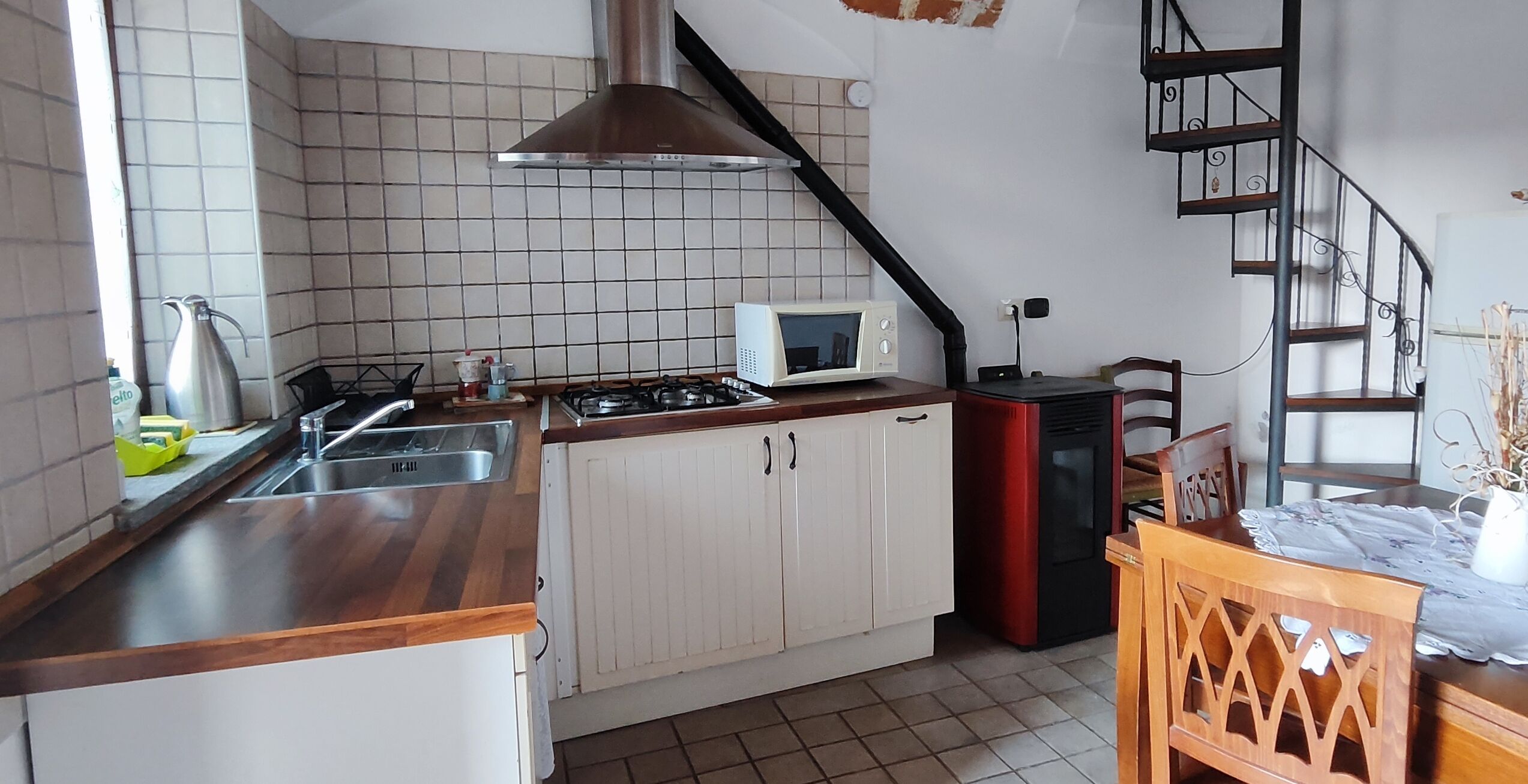 Eine kleine Küche mit weißen Schränken, einer Mikrowelle, einem Gasherd und einem roten Kühlschrank.