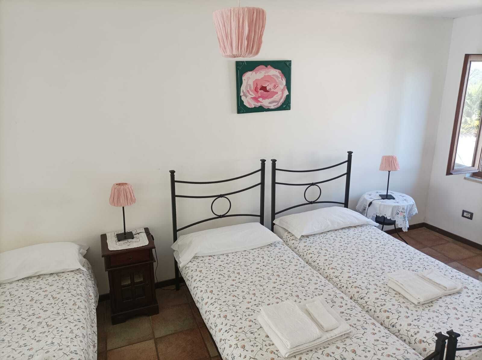 A bedroom with two single beds, a nightstand with a lamp, a small table with a lamp, and a framed picture on the wall.
