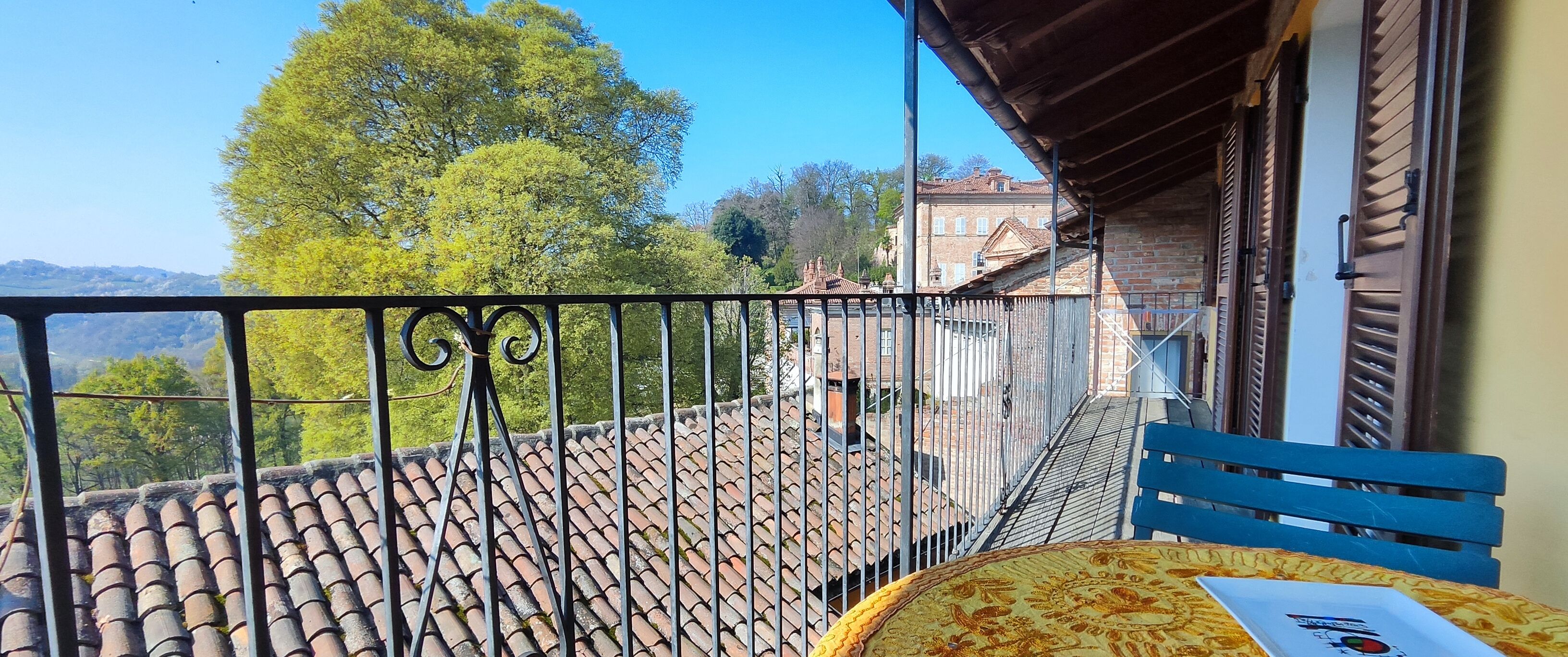 Un balcón con suelo de baldosas, un banco azul y una mesa con mantel estampado.