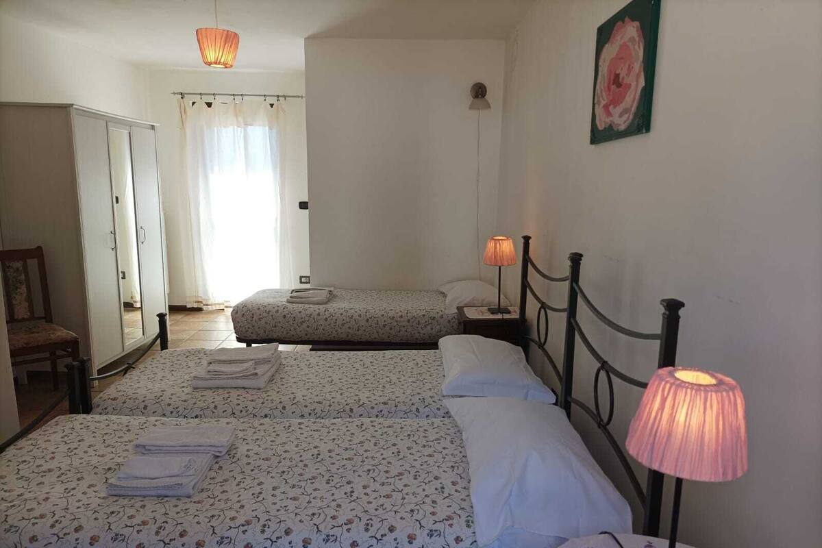 A room with two beds, a chair, a lamp, and a painting on the wall.