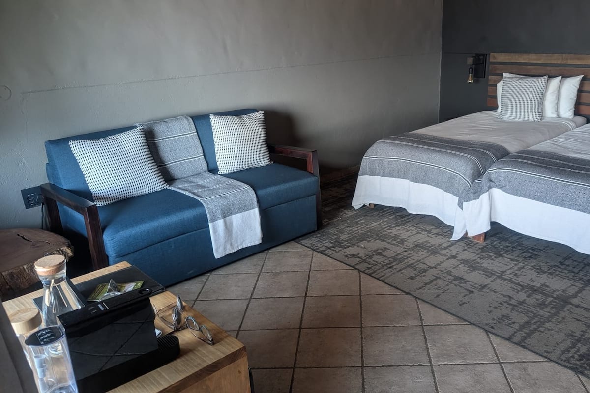A bedroom with a bed, a sofa, and a small wooden table with a bottle and glasses.