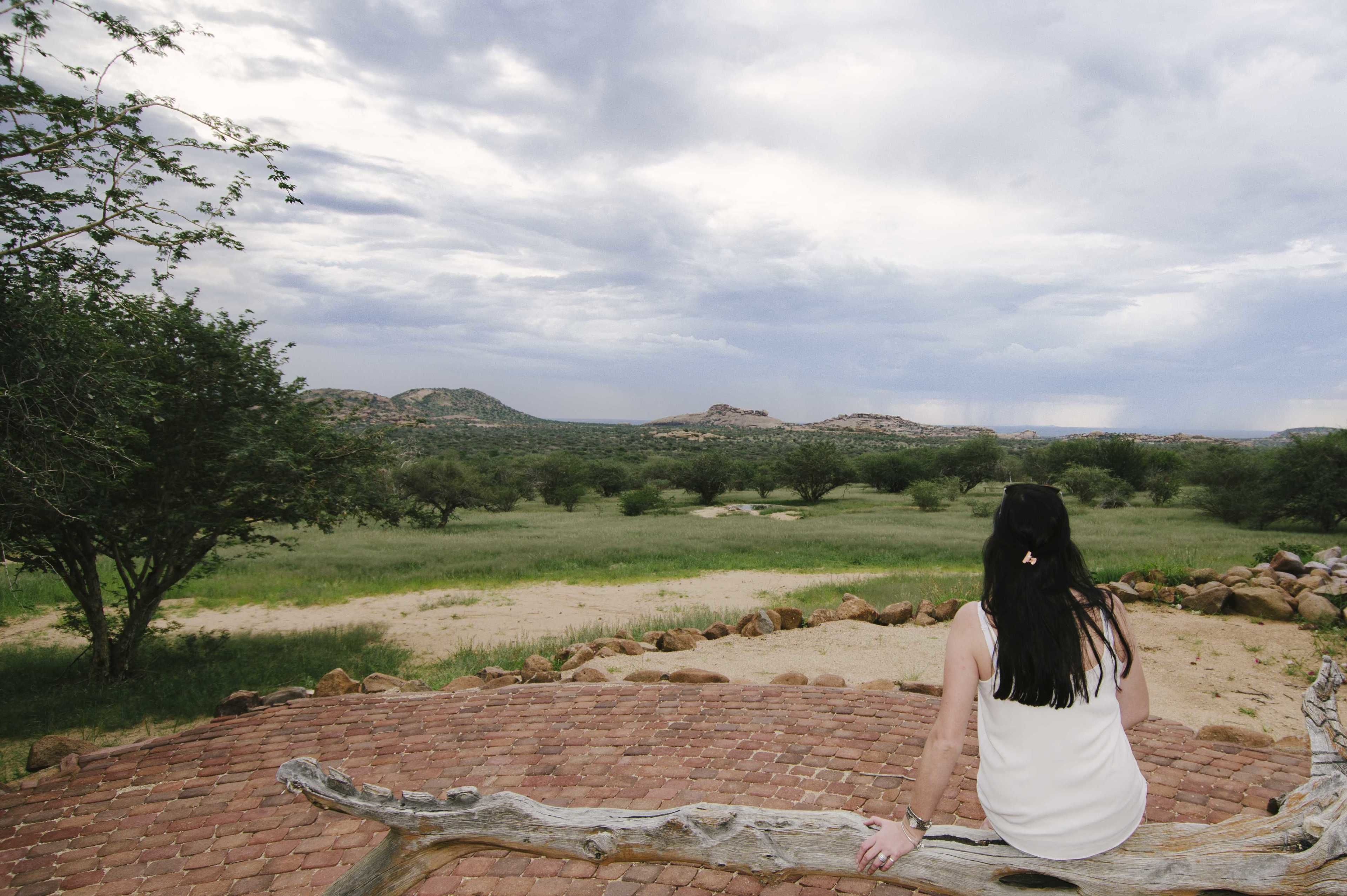 Una persona sentada sobre superficie de ladrillo, con vista a un paisaje natural.