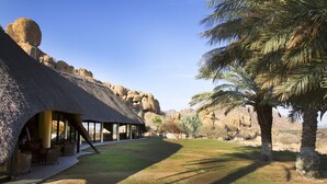 A thatched-roof building with outdoor seating, surrounded by natural rock formations and palm trees.