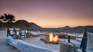 A desert landscape with a campfire, seating area, and a view of distant mountains.