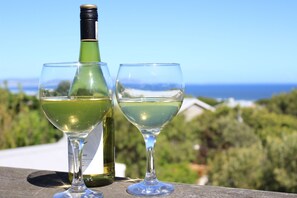 A wine bottle and two glasses on a wooden surface with a scenic view in the background. - Villa Blu (Hermanus)