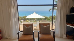 A room with two brown chairs facing a large window overlooking a pool and the ocean. - 59LongSantos (Mossel Bay)