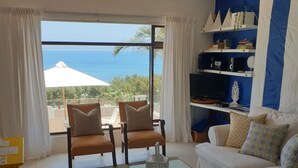 A living room with a white sofa, two armchairs, a coffee table, and a bookshelf. There is a view of the ocean through large windows. - 59LongSantos (Mossel Bay)