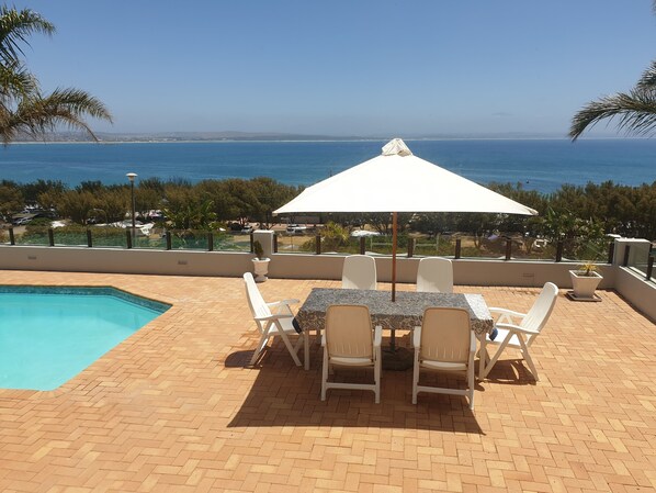 A poolside area with a table and chairs, a white umbrella, and a view of the ocean.