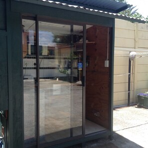 A building with a sliding glass door entrance, a wooden exterior, and a visible outdoor area with a concrete floor. - Cottage in Orange Grove (Johannesburg)
